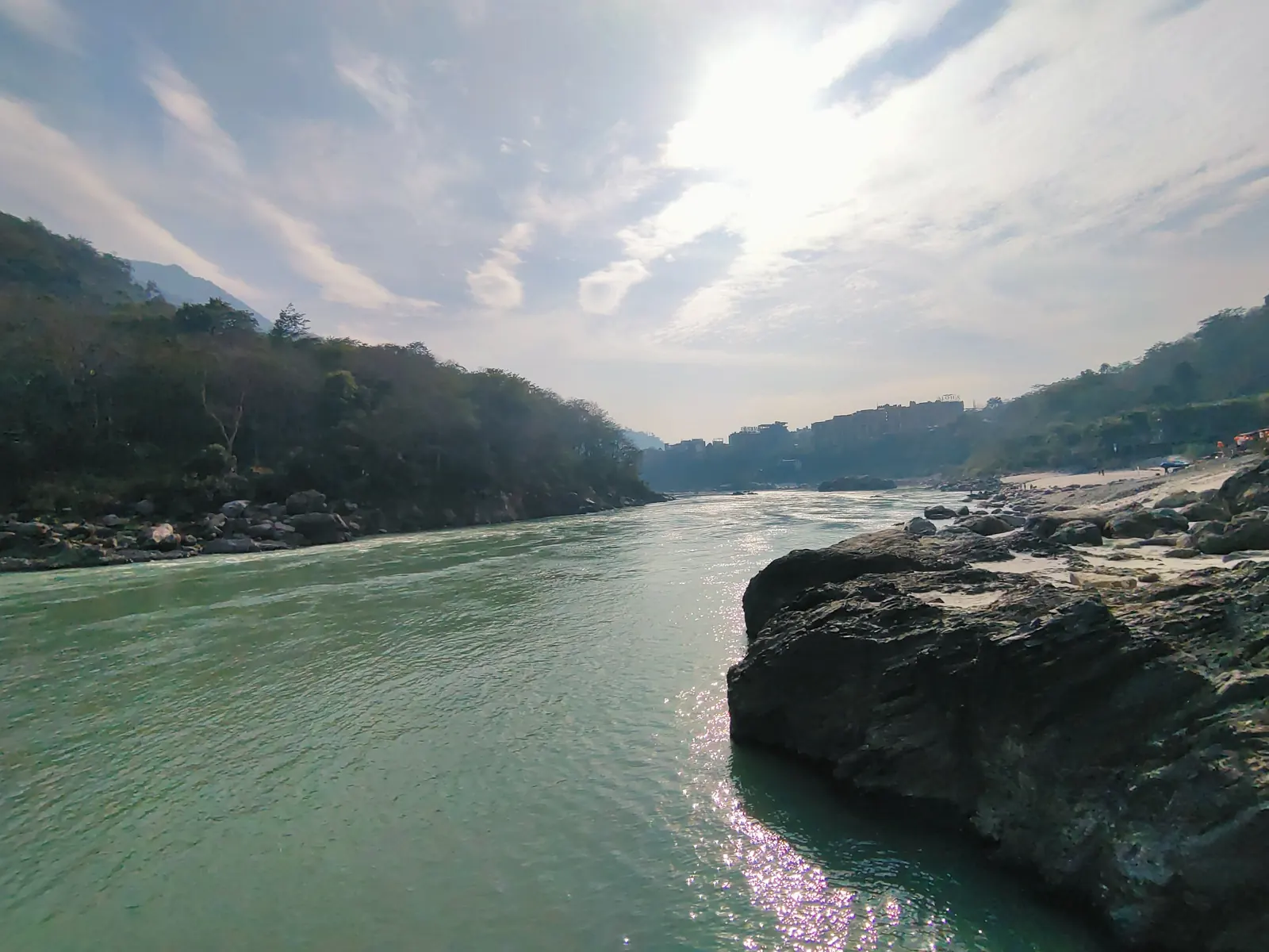 Sunlight sparkling on the Ganga beside a large boulder